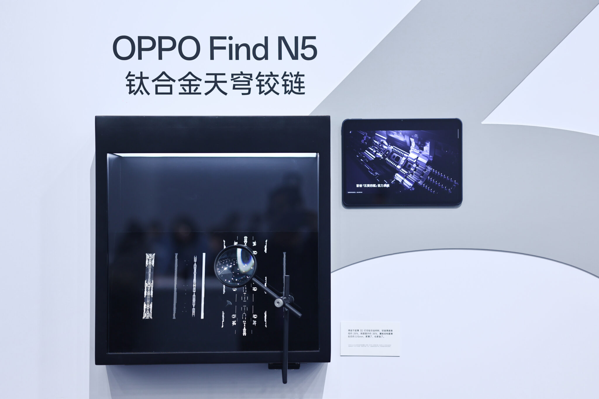 Exhibition wall display of titanium additive foldable-device hinge mechanism blanks under a magnifier