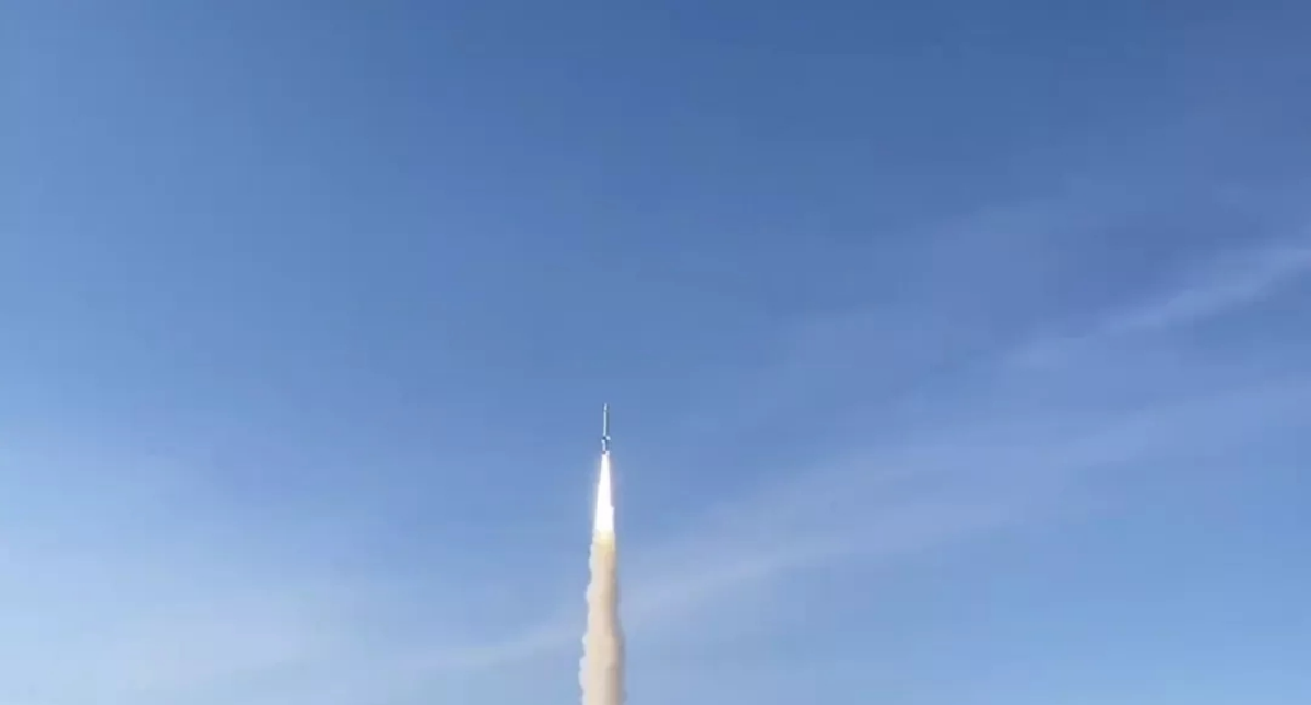Launch vehicle ascending with a bright exhaust trail against a clear blue sky
